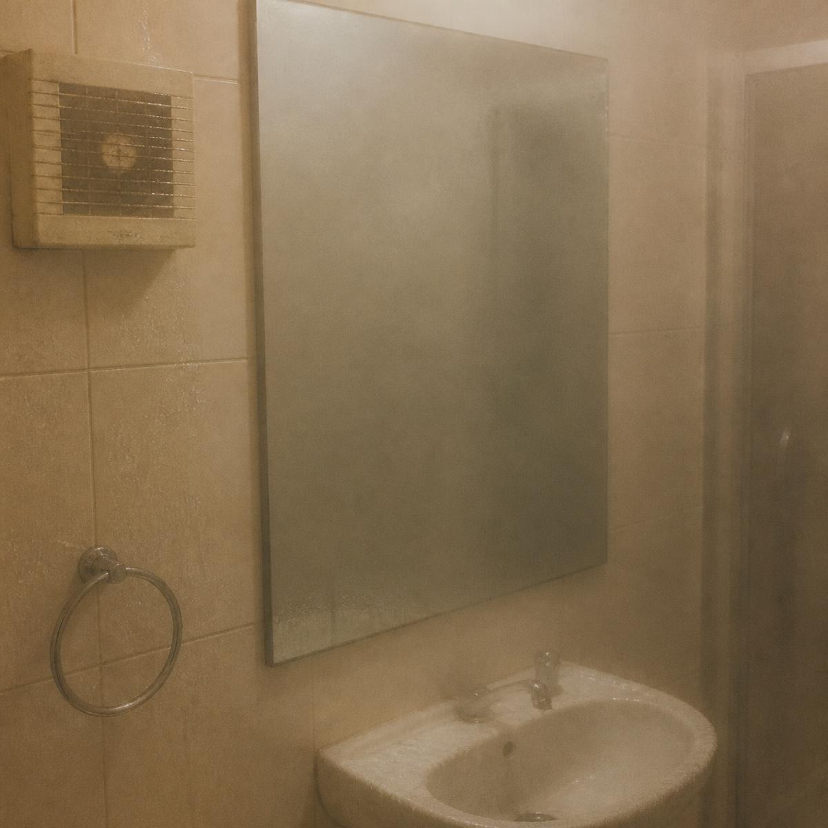 A steamed-up bathroom with a fogged mirror and an old wall extractor fan